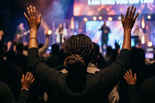 Church congregation worshipping with hands raised during a live Sunday service with worship presentation software displayed on screen.